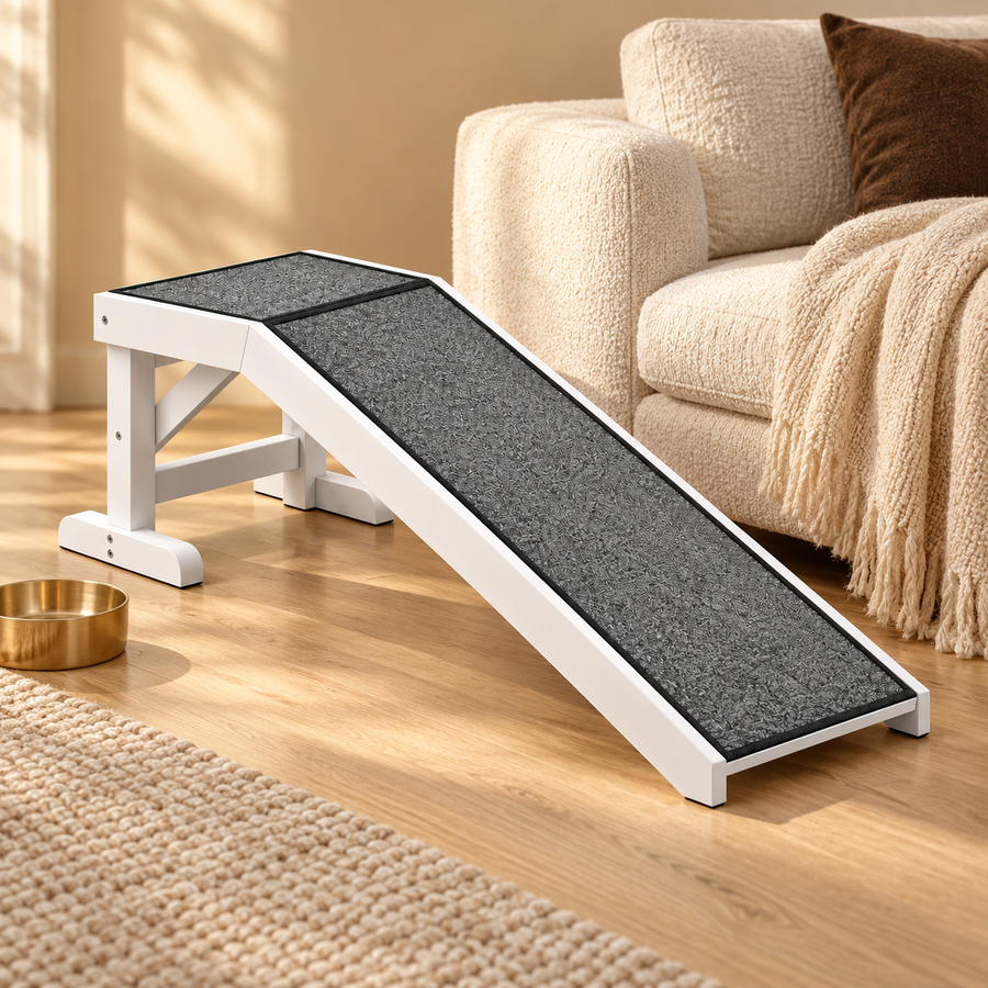 White wood pet ramp with a gray carpeted slope placed by an armchair next to a brass bowl on a wood floor
