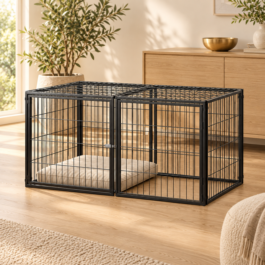 Empty low black wire dog kennel with a linen cushion beside an oak sideboard and potted plant in a cream room
