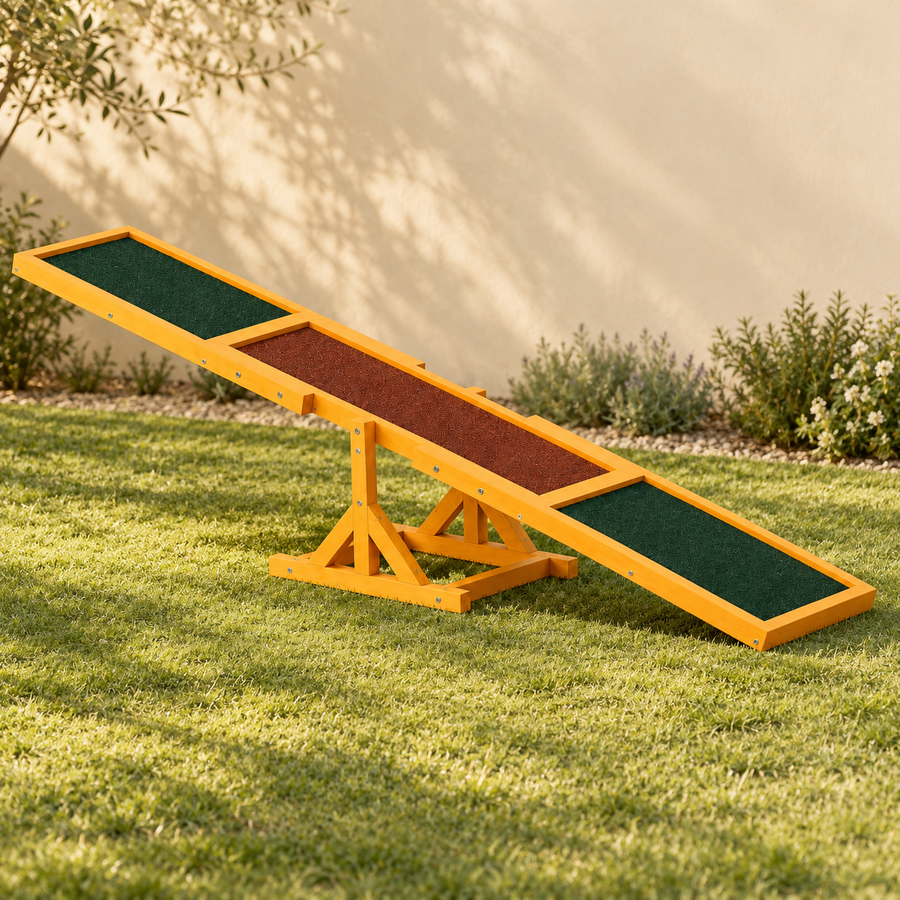 Wooden dog agility seesaw standing alone on a lawn, with green end panels and a brown center above its braced base.