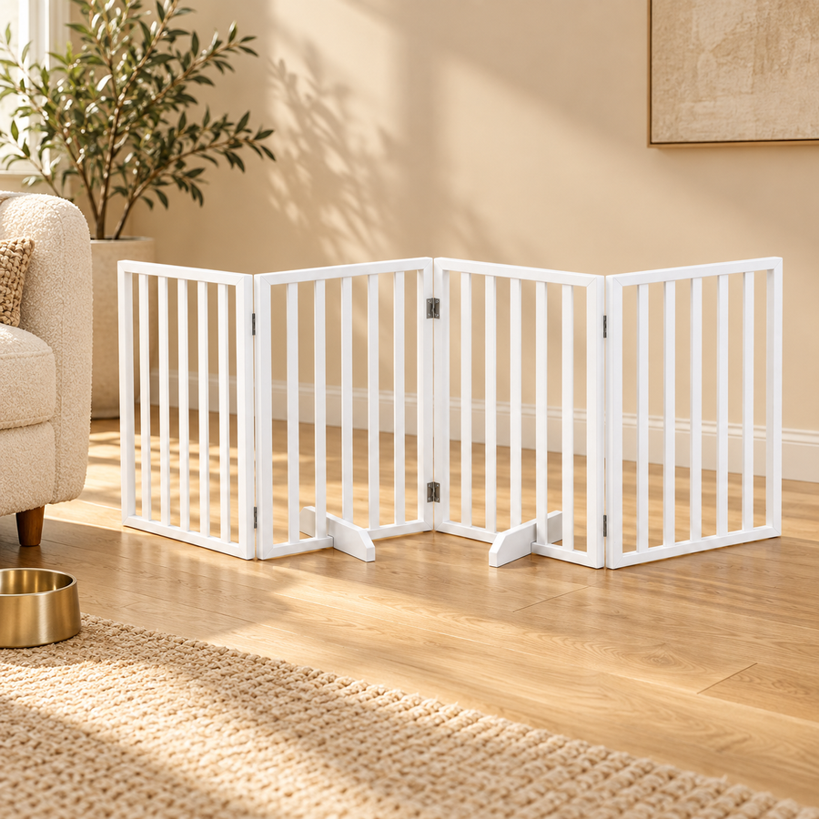 White four-panel folding pet gate standing on a wood floor beside an armchair and gold bowl