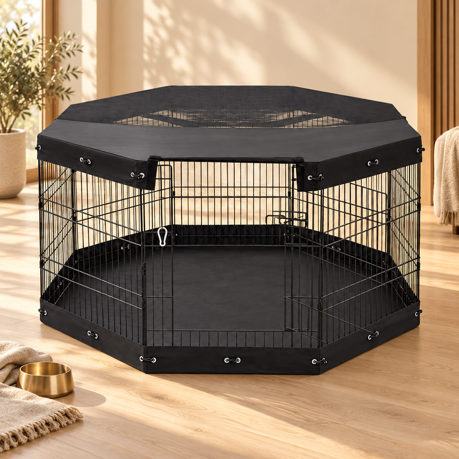 Black eight-panel covered dog playpen with a floor mat on a wood floor beside a brass food bowl