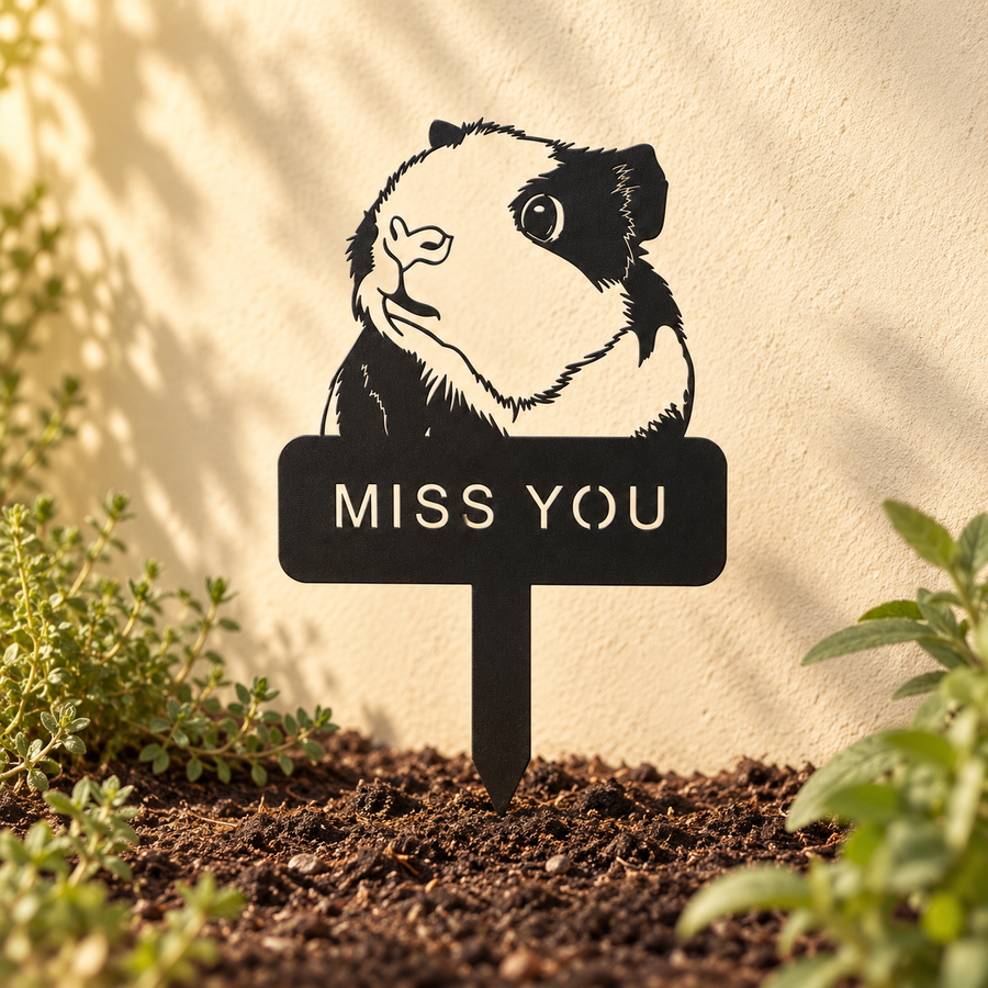 Black guinea pig memorial stake set in dark soil beside a cream garden wall in soft daylight