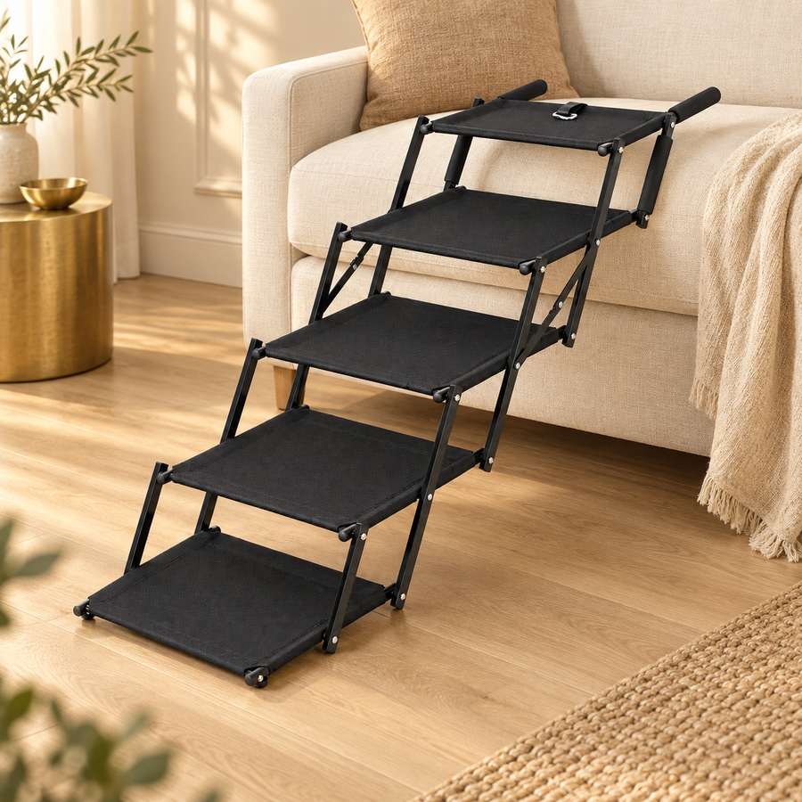 Five-step black foldable dog stairs standing on a wood floor against a cream sofa