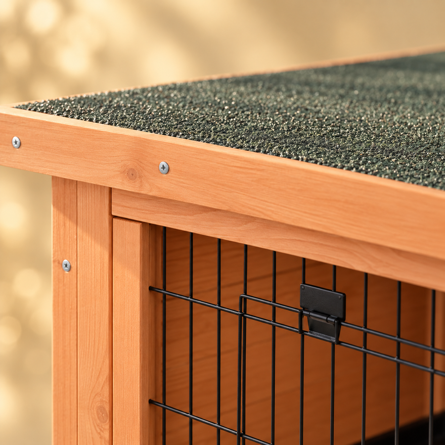 Close-up of the green asphalt roof edge, fir-wood frame and black wire door latch of a wooden rabbit hutch