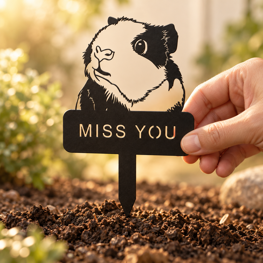 Hand placing a black guinea pig memorial stake with a MISS YOU plaque into garden soil