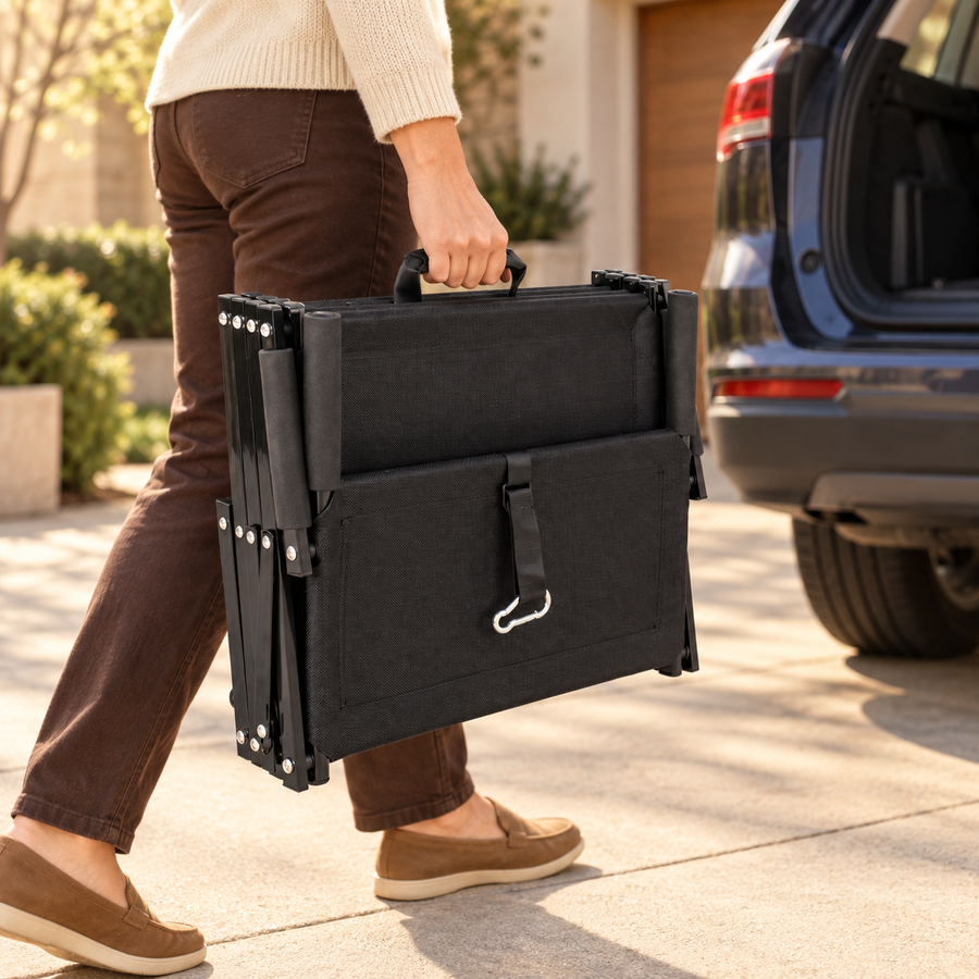 Person carrying folded black dog stairs by the handle with a carabiner strap past an SUV