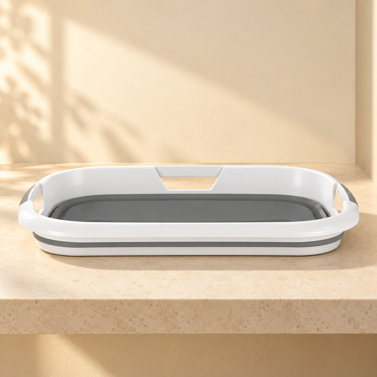 The gray and white pet bathtub folded flat on a pale stone counter, showing its low profile and rim openings.