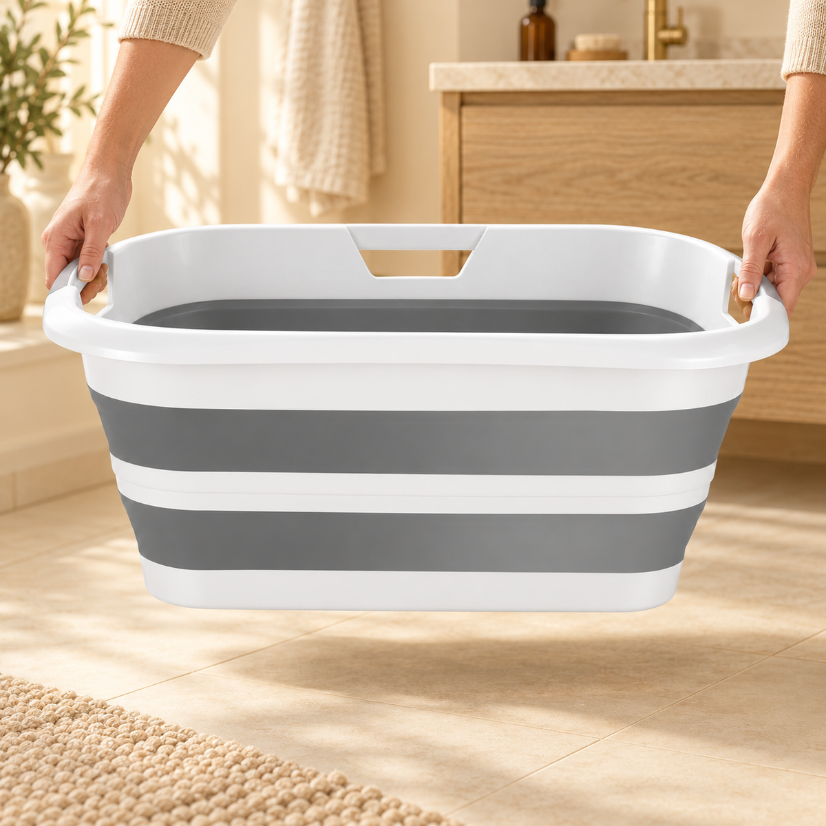 Adult hands lift the empty gray and white pet bathtub by its molded rim grips above a pale tiled floor.