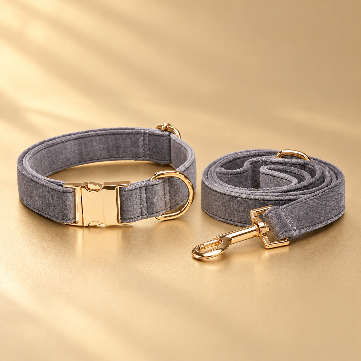 Gray velvet collar and matching rolled leash arranged with blank gold-tone fittings on a champagne surface