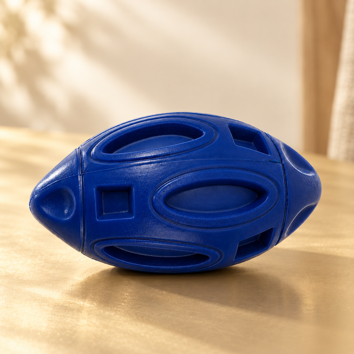 Single navy rubber football dog toy on a warm champagne surface with its textured side facing forward