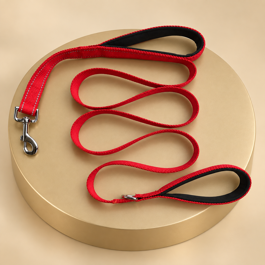 Red nylon dog leash with two padded handle loops and a swivel clip coiled on a round plinth